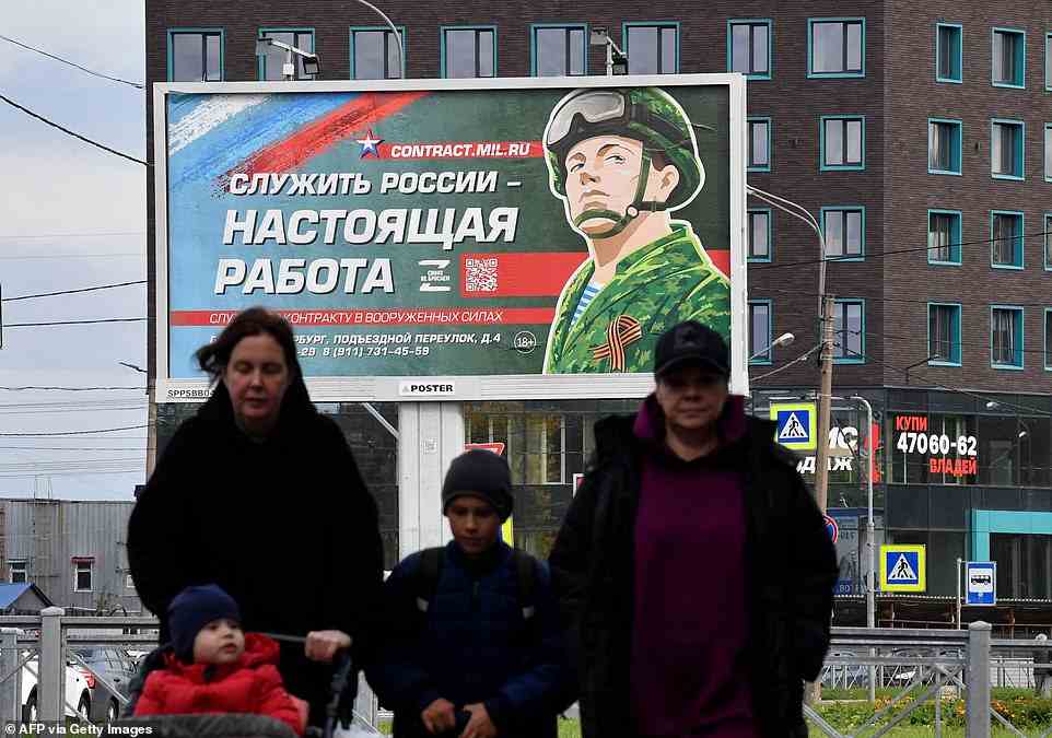 A family walks in front of a billboard promoting the military in St Petersburg, with the slogan: 'Serving Russia is a real job'
