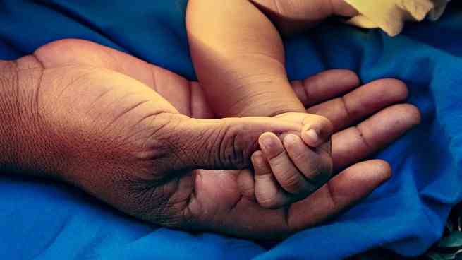 Die Hand eines Babys hält den Daumen eines Erwachsenen