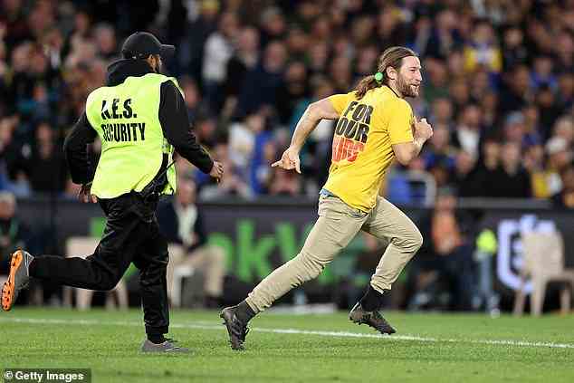 The protester - who wore football boots to give him traction while running onto the grass surface - grins as he runs away from a pursuing security guard.