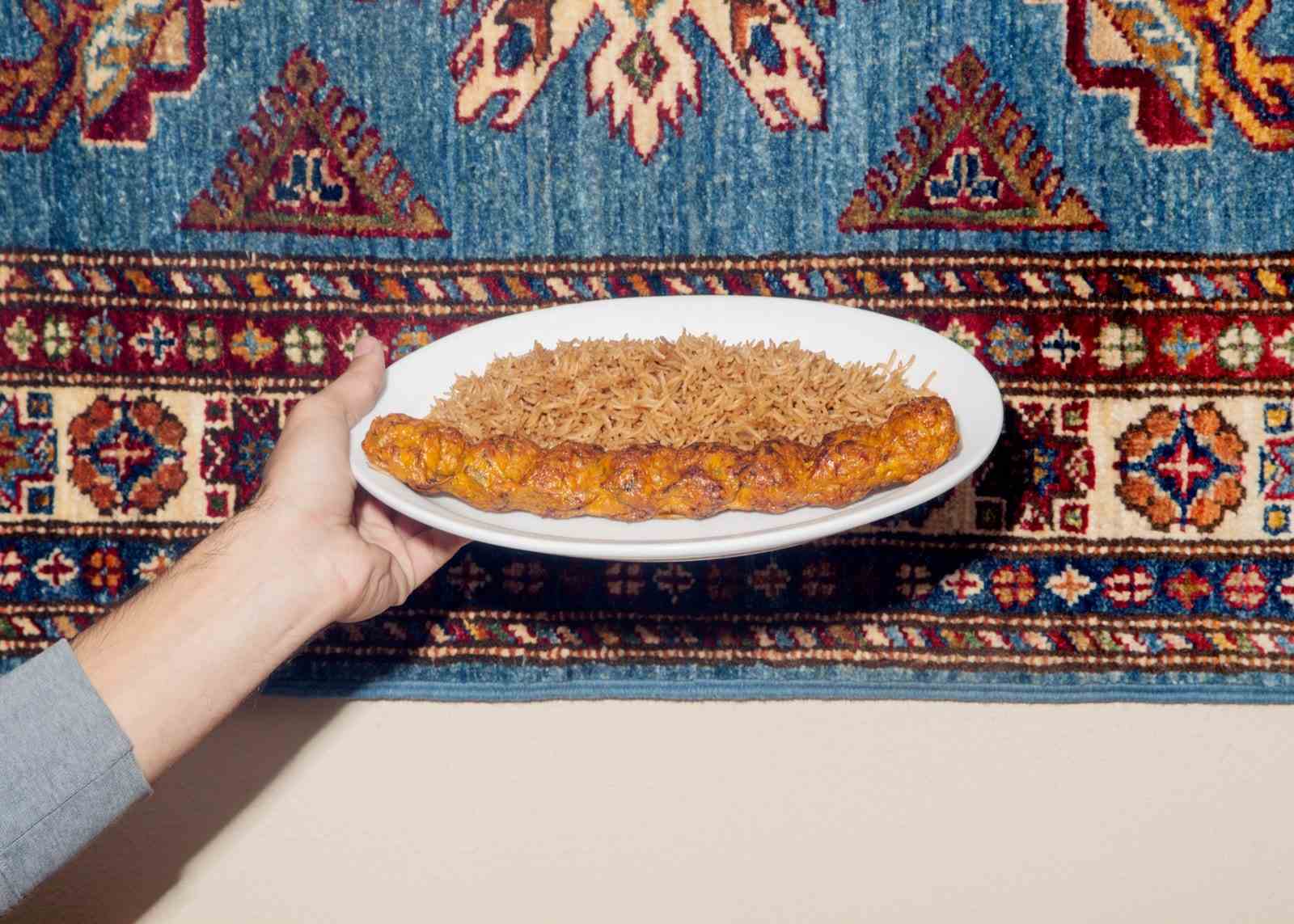 Eine Hand hält einen Teller mit Groundchickenkofta-Kebab mit Reis.