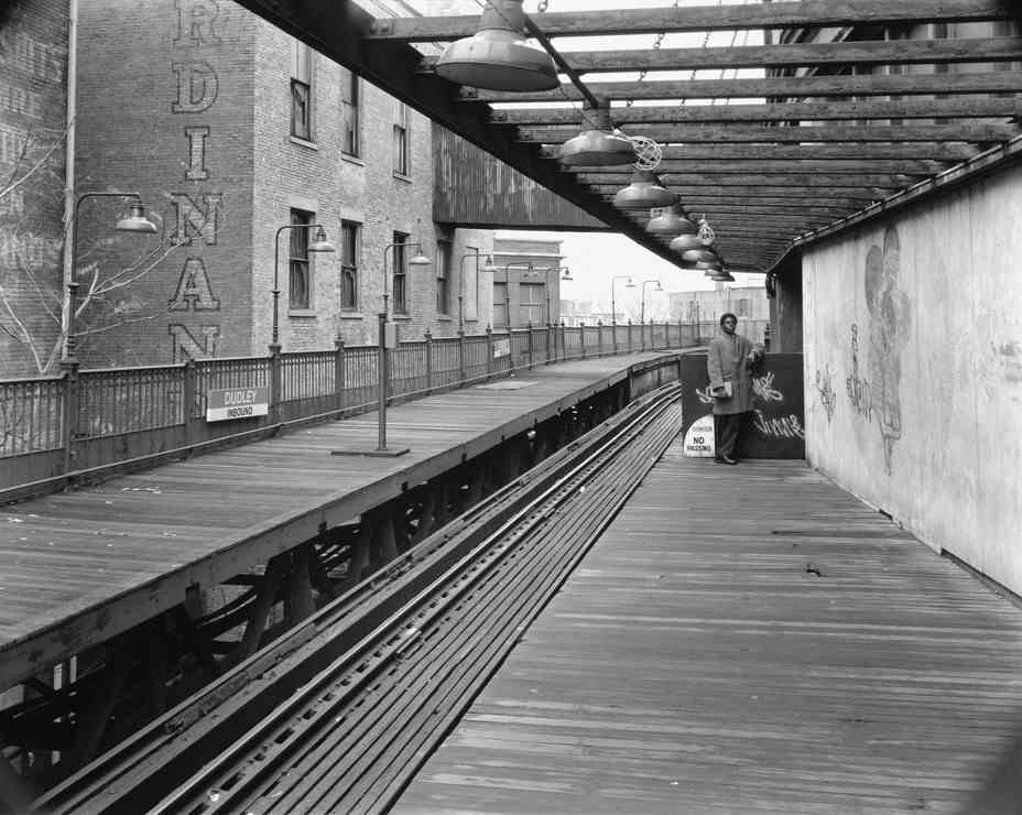 Schwarz-Weiß-Foto eines fast leeren Bahnsteigs mit einer Person, die am anderen Ende im Mantel steht