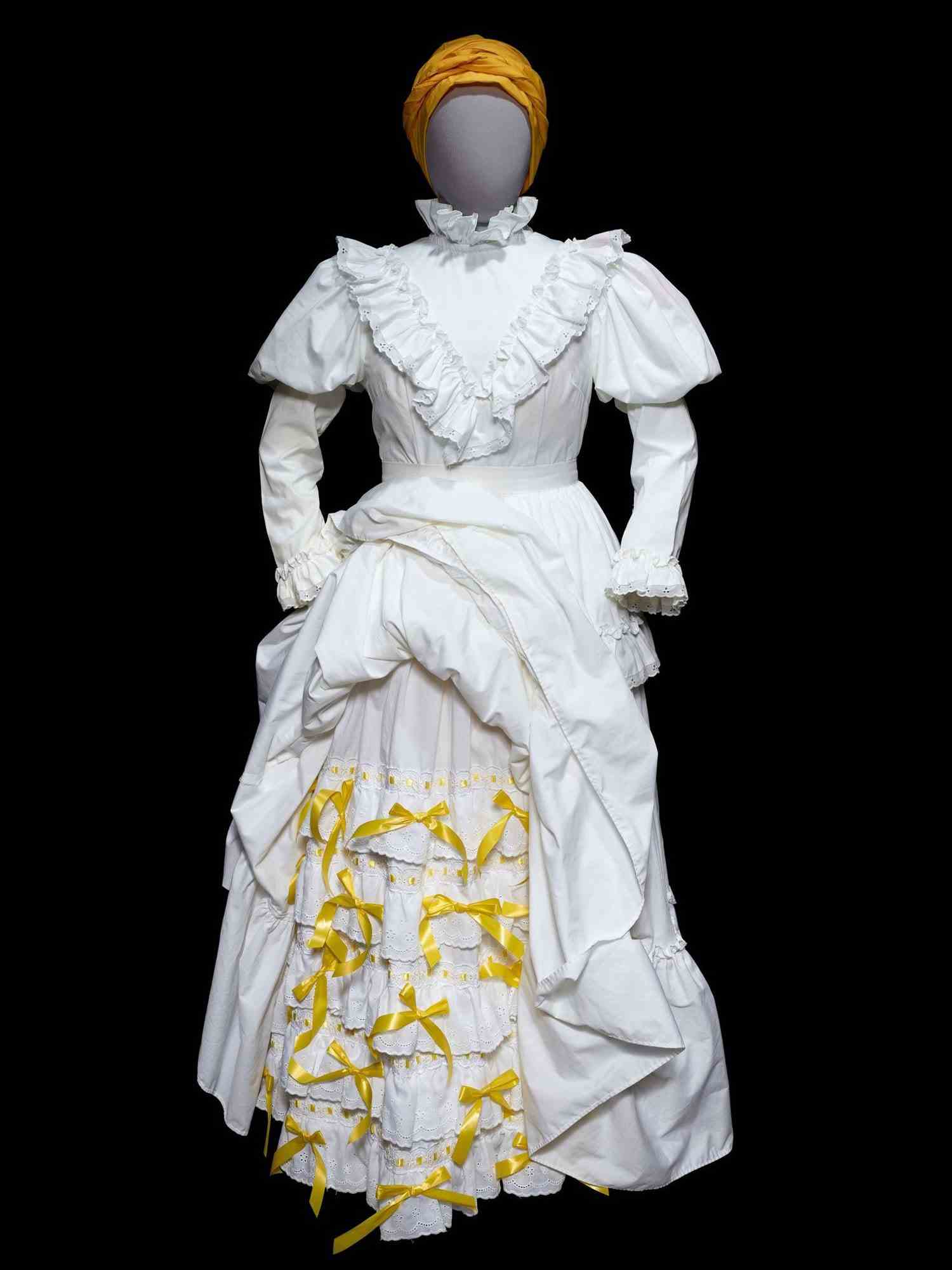 Weißes Kleid mit Rüschen und gelben Details mit gelbem Hut auf Mannequin.