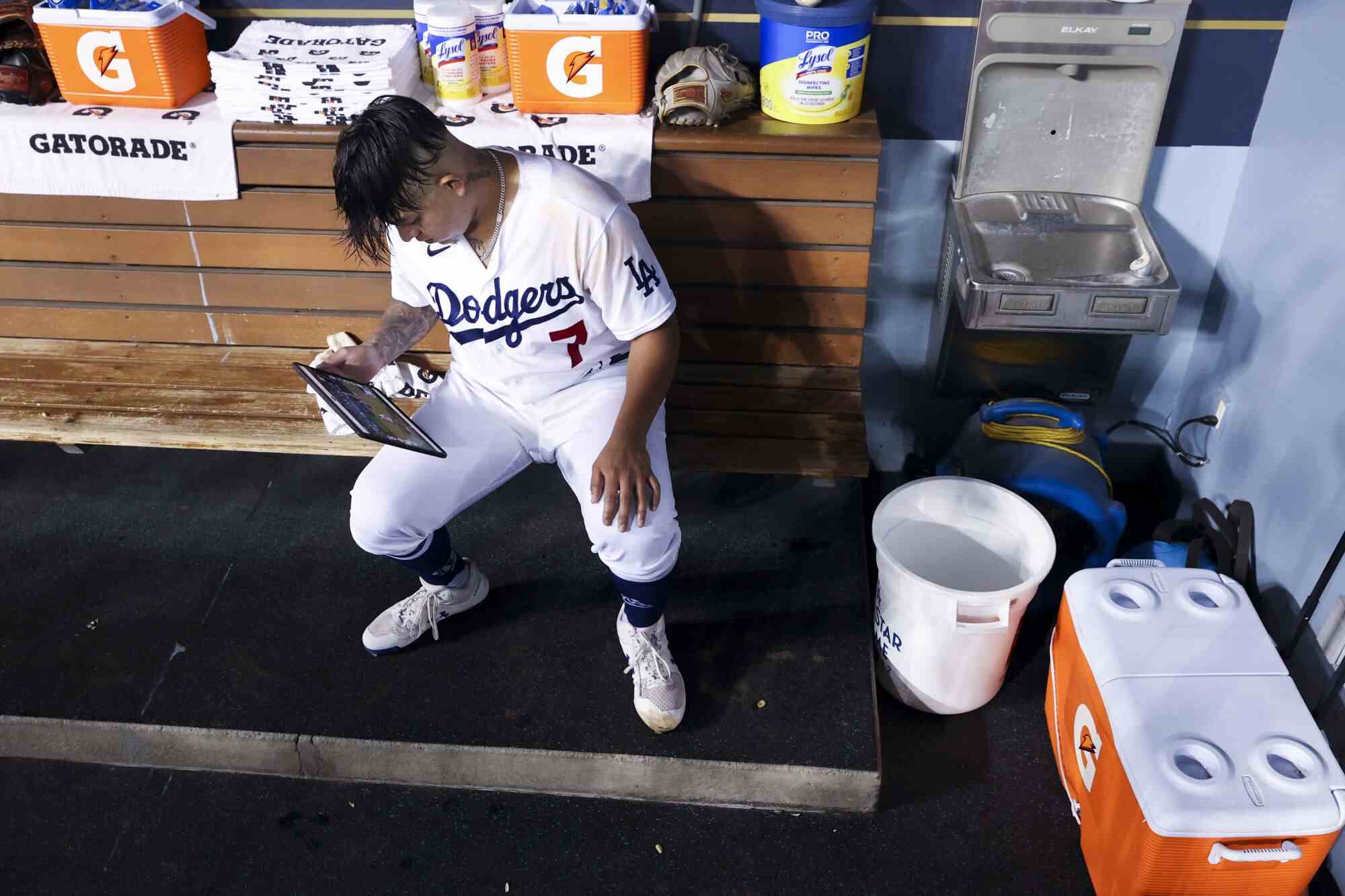 Dodgers-Starting-Pitcher Julio Urías sitzt auf der Trainerbank und schaut sich die Spiele mit einem Tablet an.