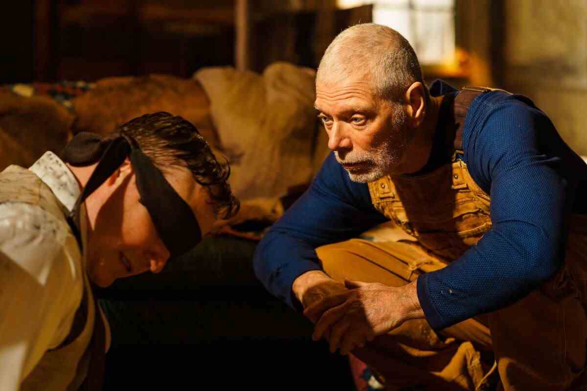 Ein Mann im Overall hockt im Film neben einem Mann mit verbundenen Augen "Alter Mann."