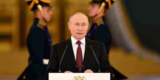 Wladimir Putin hält eine Ansprache, flankiert von Männern in Militäruniformen.