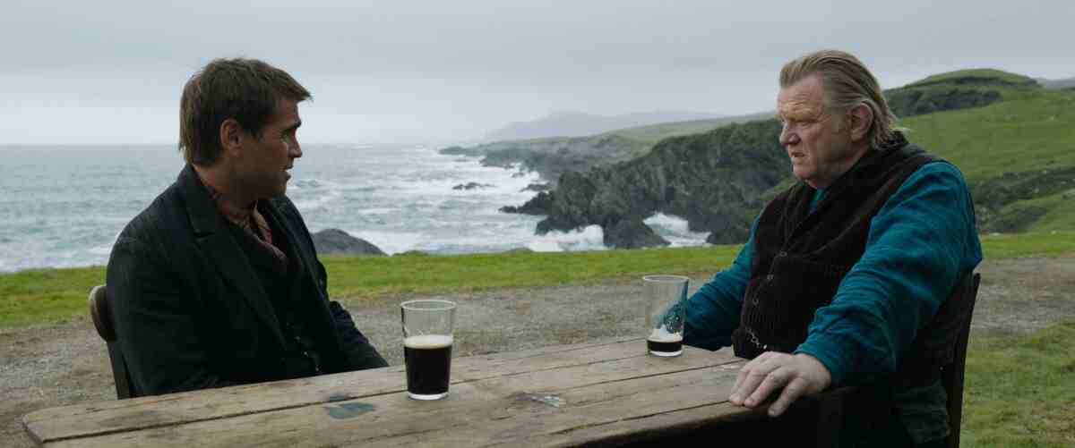Zwei Männer sitzen an einem Holztisch und trinken ein Pint vor Meereskulisse "Die Todesfeen von Inisherin."