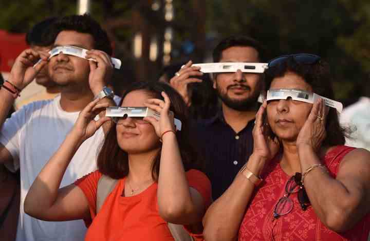 Menschen beobachten die partielle Sonnenfinsternis durch eine Schutzbrille in Neu-Delhi, Indien.