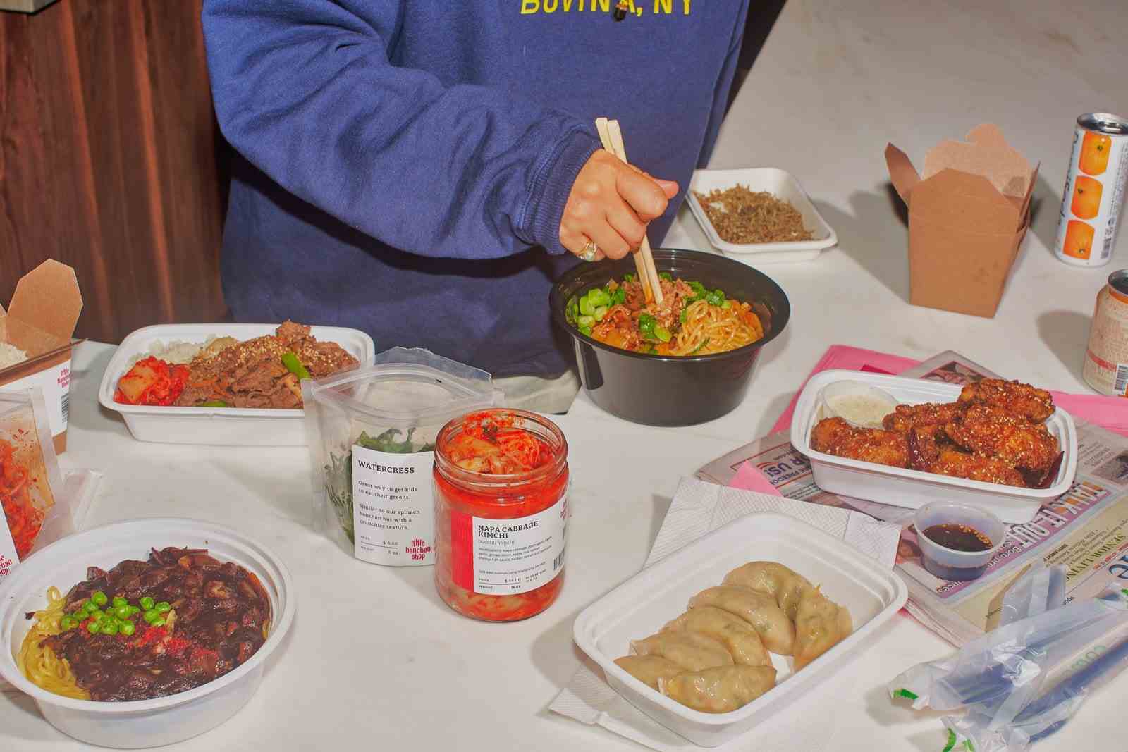Eine Hand rührt eine Schüssel Jjamppong-Rindfleisch-Nudelsuppe auf einem Tisch mit anderen Gerichten und Beilagen