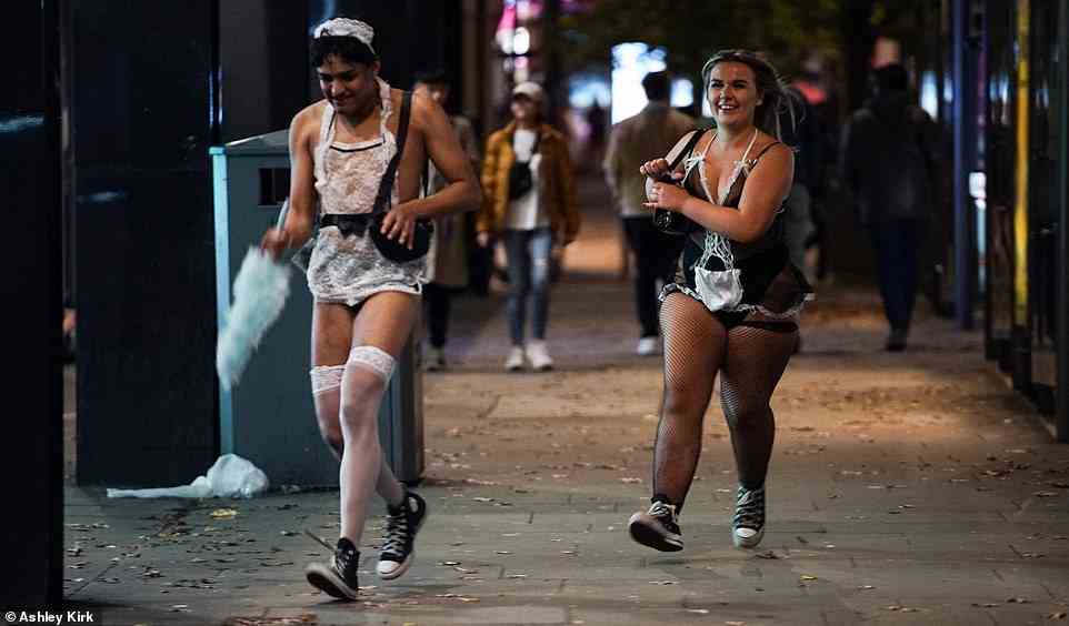 Two partygoers dressed in frilly maid outfits run along the street in Nottingham city centre