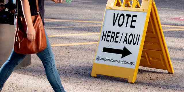 Ein Bewohner geht an einem vorbei "Stimmen Sie hier ab" Schild vor einem Wahllokal in der Burton Barr Central Library in Phoenix, Arizona.