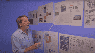 Foto des Spieledesigners Will Wright, der einen Zeiger hält und sich Diagramme zu seinem neuen Spiel ansieht