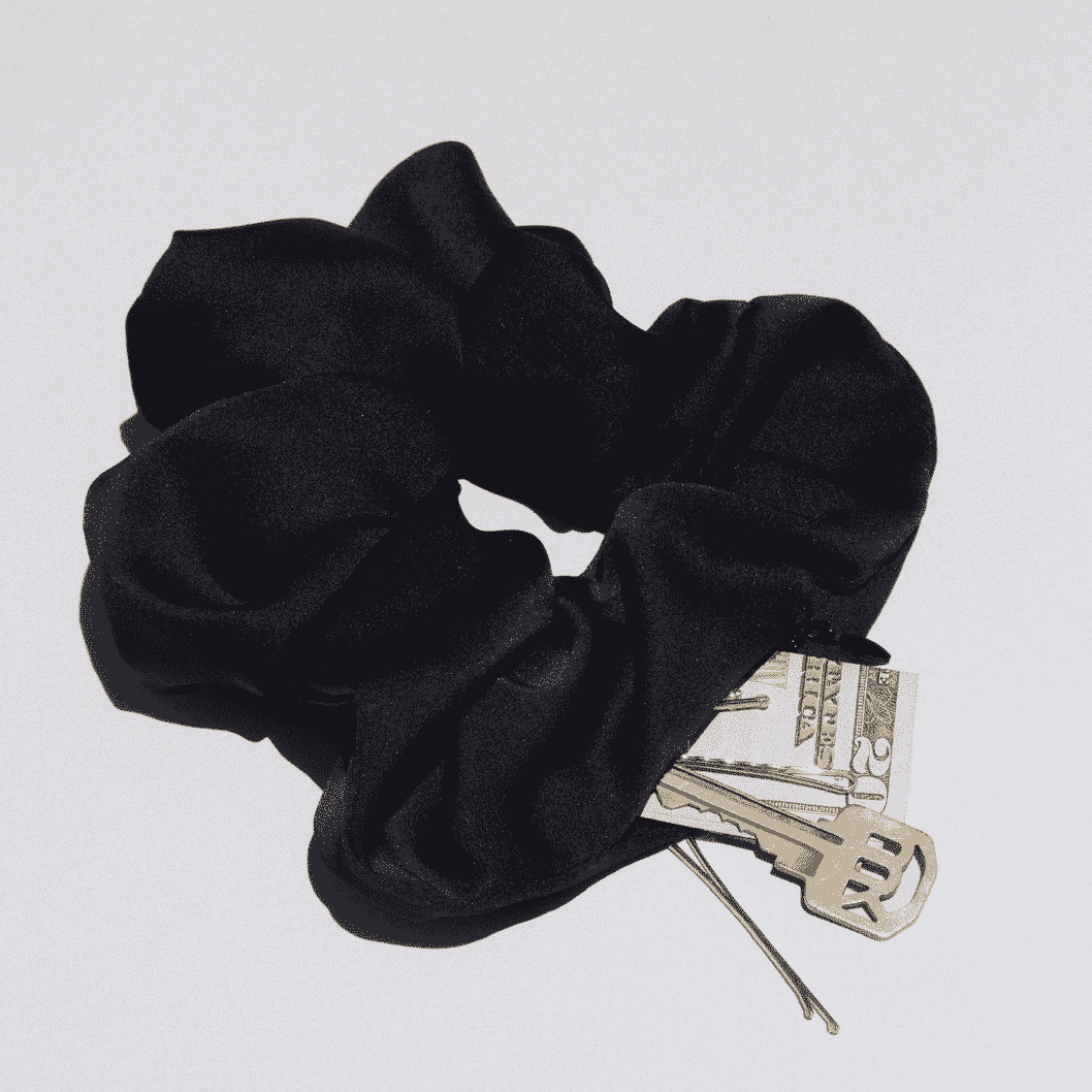 Kristin Ess The Zipper Pocket Scrunchie Schwarzes Scrunchie mit Geld und Schlüssel auf grauem Hintergrund