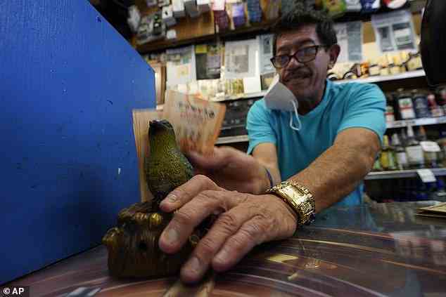 Kassierer Ronald Francisco Marin reibt am Samstag, den 5. November 2022 im Bluebird Liquor Store in Hawthorne, Kalifornien, Lottoscheine auf der Rückseite eines Bluebirds