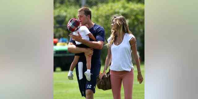 Der Quarterback der New England Patriots, Tom Brady, trägt seinen Sohn Benjamin, als er am Ende des Trainings mit Gisele Bundchen das Trainingsfeld verlässt.  (John Tlumacki/The Boston Globe über Getty Images)