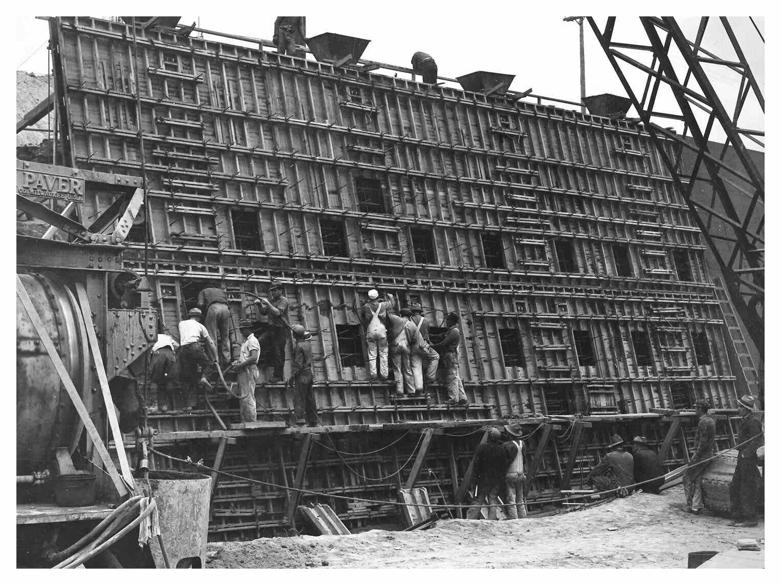 Historical black and white image of construction workers standing on scaffolding pouring concrete into wooden-form windows to start the channelization of the L.A. River.