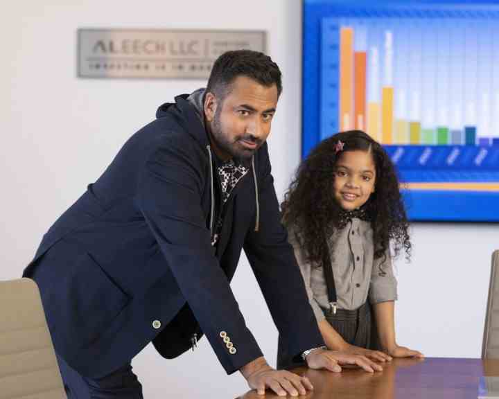 Kal Penn und Rupali Redd lehnen in einer Szene aus „Die Weihnachtsmänner“ an einem Schreibtisch.