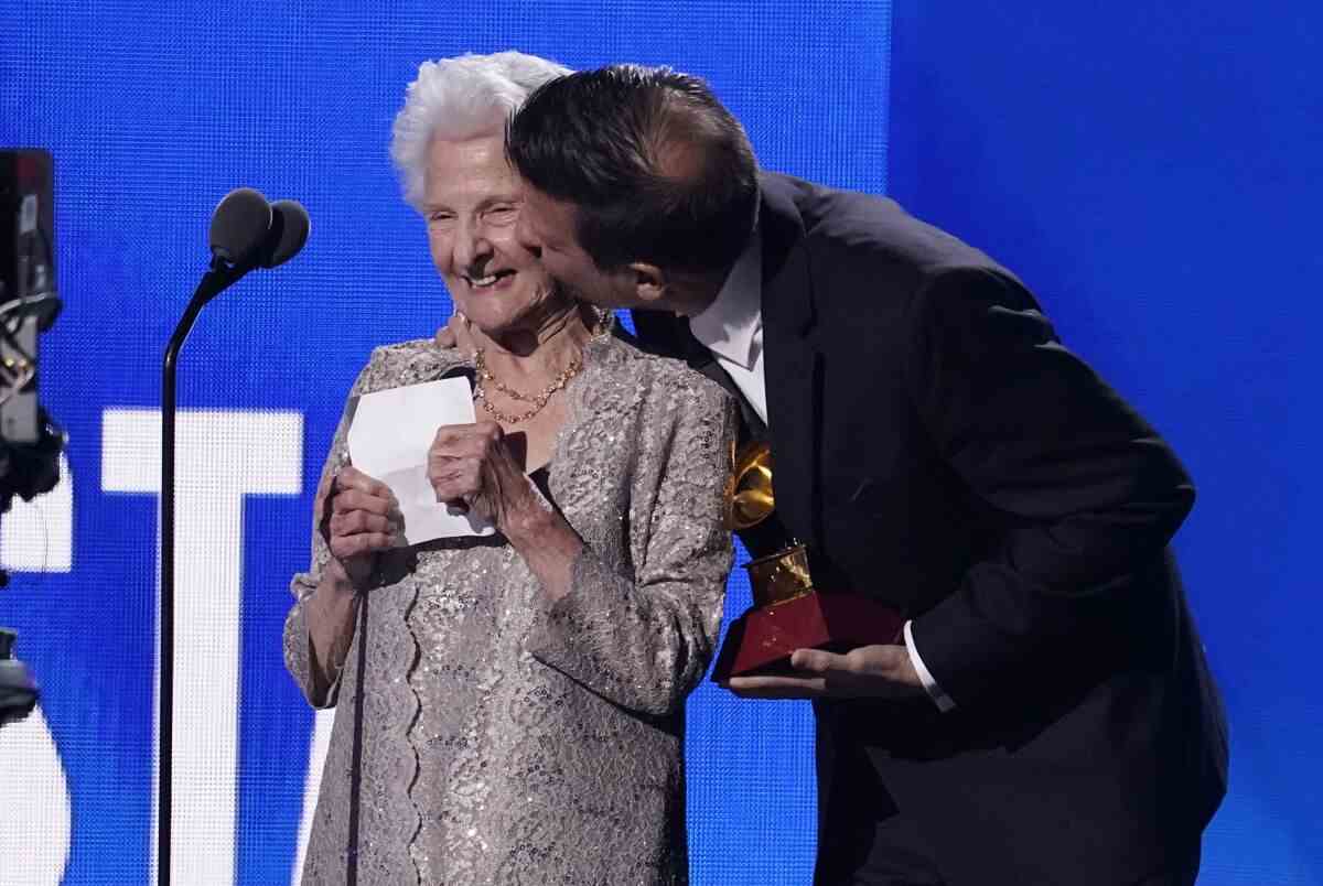 Eine ältere Frau bekommt einen Kuss auf die Wange, während sie auf der Bühne einen Preis entgegennimmt