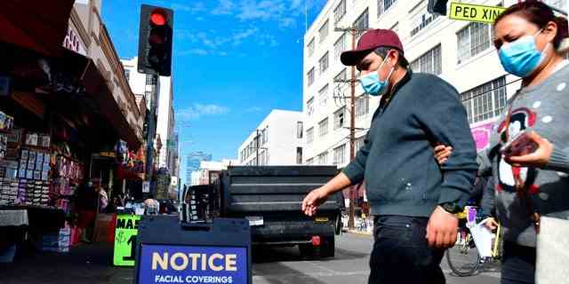 Ein Schild erinnert die Menschen an die Pflicht zur Gesichtsbedeckung, da Fußgänger am 12. November 2020 in Los Angeles, Kalifornien, aufgrund des Coronavirus Gesichtsmasken tragen. 