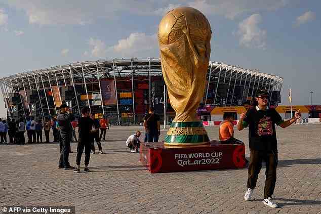Menschen posieren für Fotos neben einer riesigen Nachbildung des WM-Pokals vor dem Stadion 974