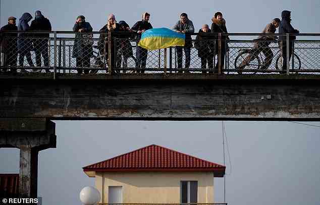 Menschen warten auf die Ankunft des ersten Zuges aus Kiew und halten die ukrainische Flagge über die Eisenbahnbrücke