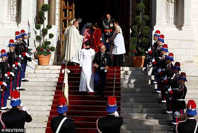 Charlene entschied sich für Monacos Nationalfeiertag für einen langen, weißen Mantel, der über einem hochgeschlossenen schwarzen Kleid getragen wurde.  Sie zog auch ein Paar schwarze Lederhandschuhe an