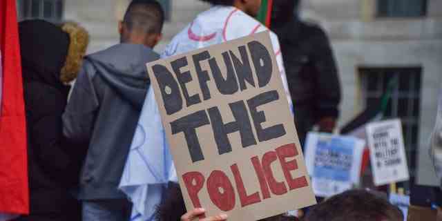 Ein Demonstrant hält ein Plakat mit der Aufschrift „Defund The Police“.