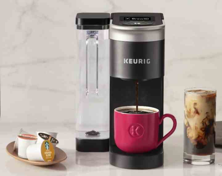 Eine Keurig K-Supreme-Kaffeemaschine steht auf einer Küchentheke neben K-Cups und einem Glas Eiskaffee.