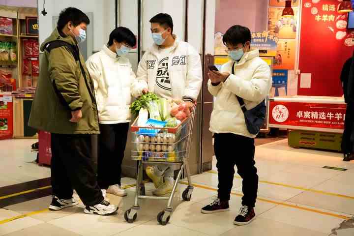 Bewohner, die Masken tragen, warten am Samstag, 26. November 2022, in der Nähe eines Einkaufswagens mit Lebensmitteln in einem Supermarkt in Peking. 