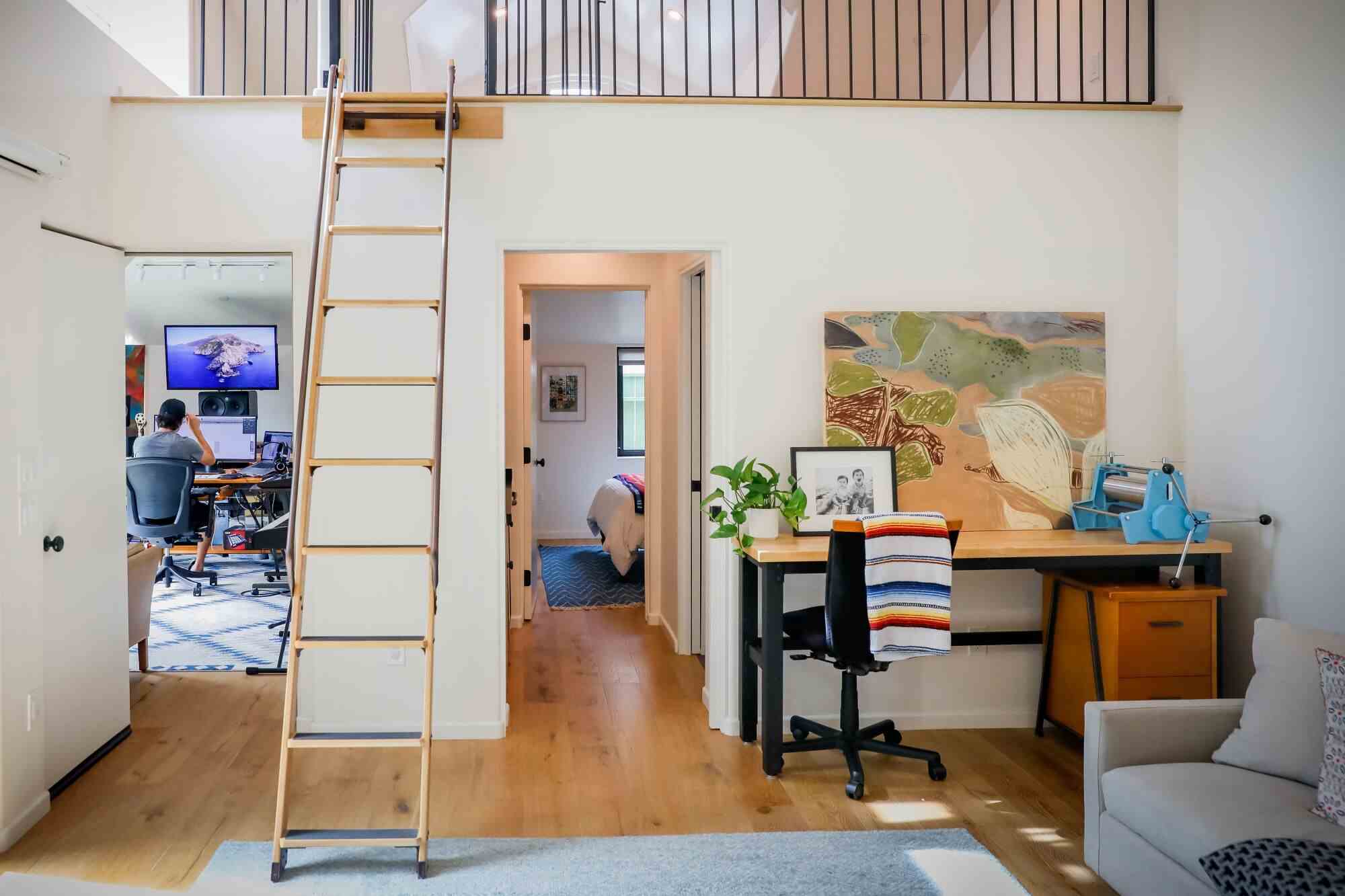 Blick auf eine Leiter, die zu einem Dachboden führt, und eine Tür, die zu einem Büro führt, in dem ein Mann neben dem Dachboden arbeitet