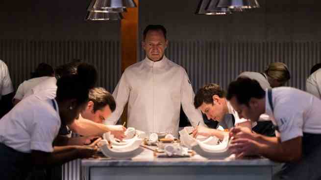 Ralph Fiennes als Chef Slowik, der an einem Küchentisch den Vorsitz führt "Die Speisekarte"