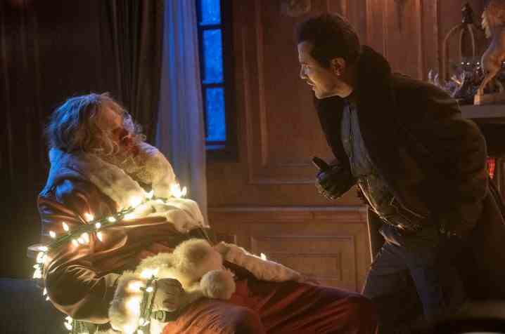 David Harbous ist als Weihnachtsmann verkleidet und mit Weihnachtsbeleuchtung gefesselt, während John Leguizamo ihn anschreit.
