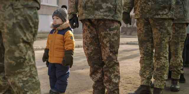 Ein Kind ahmt die Position ukrainischer Soldaten nach, die während der Nationalhymne während einer Veranstaltung zum Tag der Einheit in Sjewjerodonezk, Region Lugansk, Ostukraine, Mittwoch, 16. Februar 2022, stramm stehen. 