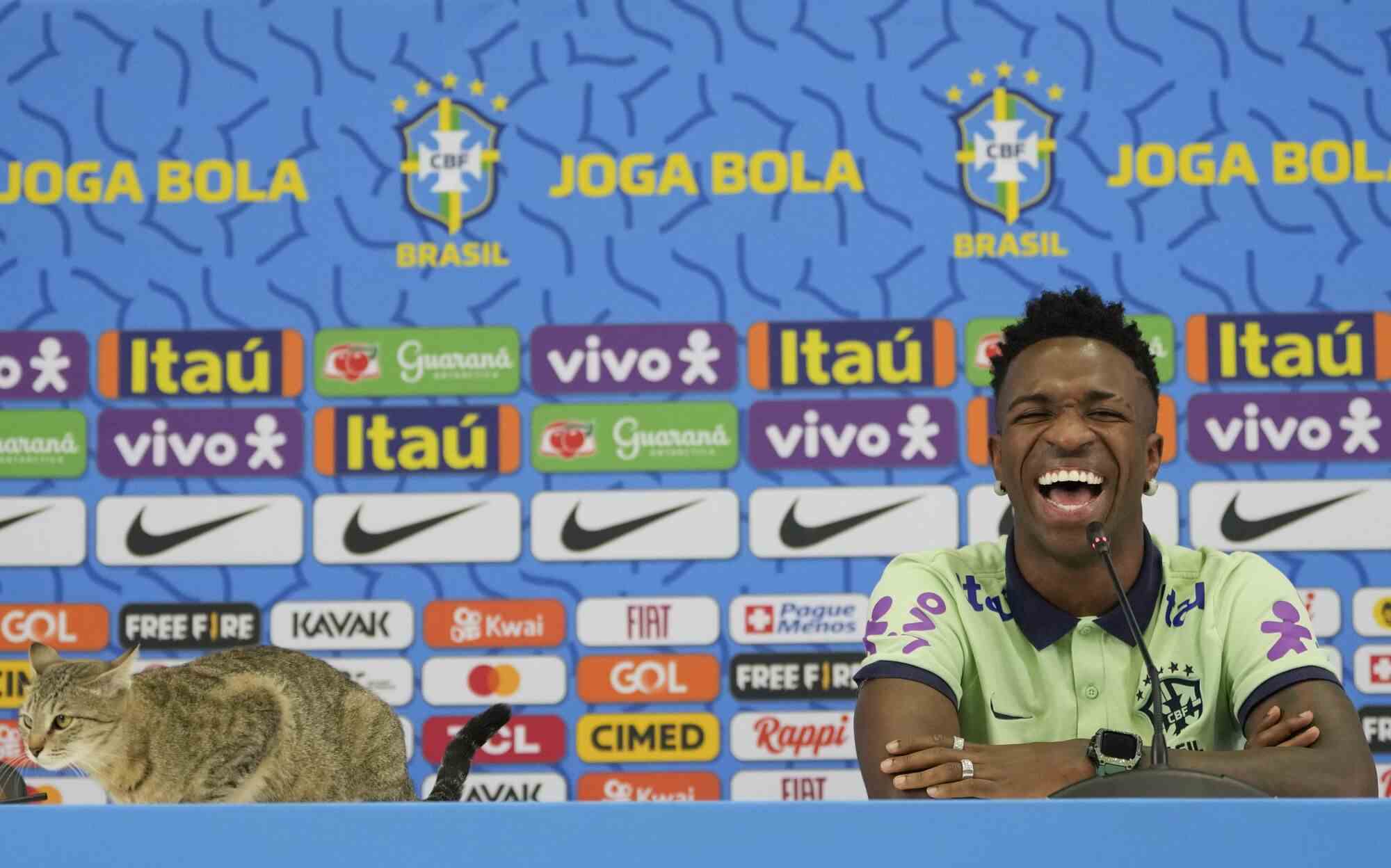 Der Brasilianer Vinicius Junior lacht, als während einer Pressekonferenz eine Katze auf dem Tisch sitzt.