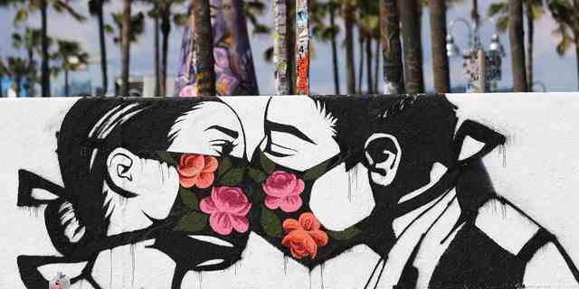 Palmen stehen hinter einem Straßenkunstwerk des Künstlers Pony Wave, das zwei Menschen zeigt, die sich küssen, während sie Gesichtsmasken tragen, am Venice Beach am 21. März 2020 in Venice, Kalifornien.