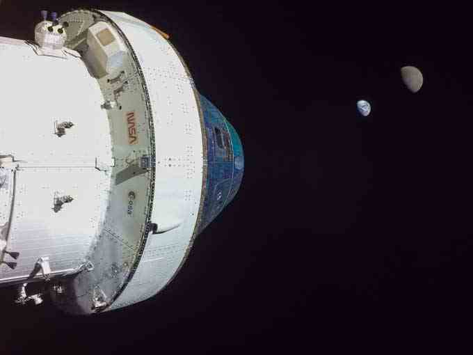 die Orion-Raumkapsel vor dem Hintergrund des Weltraums, mit Erde und Mond als winzige Halbkreise in der Ferne