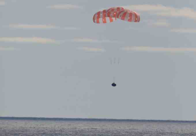 Das Orion-Raumschiff sinkt zum Pazifischen Ozean hinab, verlangsamt von einem großen rot-weißen Fallschirm