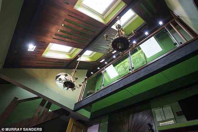 Die Wohnzimmerdecke verfügt auch über kunstvolle Holztexturen, hängende Kronleuchter und breite Dachfenster mit einer charakteristischen grünen Akzentfarbe
