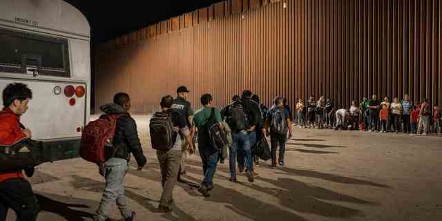 Einwanderer warten darauf, von der US-Grenzpatrouille abgefertigt zu werden, nachdem sie die Grenze von Mexiko überquert haben.  Die Grenzbarriere zwischen den USA und Mexiko ist im Hintergrund am 6. August 2022 in Yuma, Ariz. 