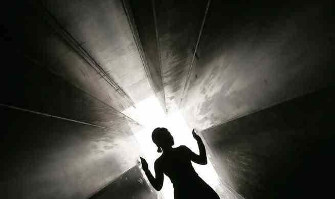 Eine silhouettierte Gestalt, die durch einen dunklen, schmalen Tunnel zum Licht geht.