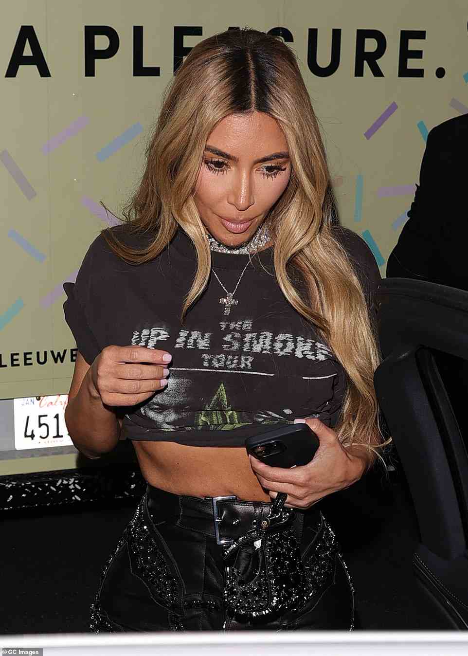 Hot: Kim Kardashian, 42, showed off her midriff in a tiny black top and high waisted leather pants as she arrived to the party. Her black hair was dyed a dirty blonde and fell in waves down the sides of her face