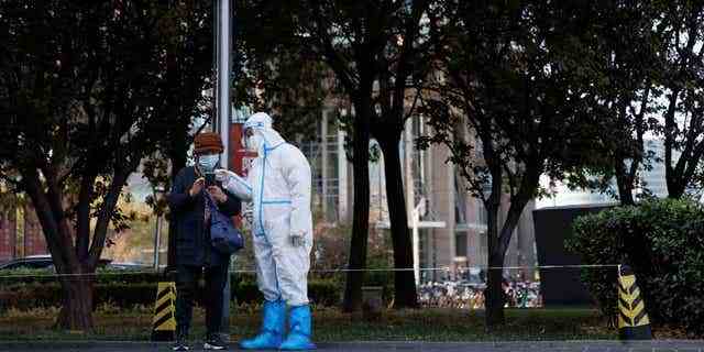 Ein Mitarbeiter der Pandemieprävention trägt einen Schutzanzug, während er die persönlichen Daten einer Frau überprüft, die sich anstellt, um einen Abstrichtest an einer Testkabine zu erhalten, während die Ausbrüche von COVID-19 in Peking am 3. November 2022 andauern. 