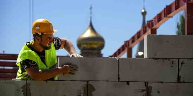 Ein Bauarbeiter arbeitet auf dem Gelände des neuen städtischen medizinischen Zentrums in Mariupol mit einer orthodoxen Kirche im Hintergrund, in einem Gebiet unter der Kontrolle der Regierung der Volksrepublik Donezk in der Ostukraine, Mittwoch, 13. Juli 2022.