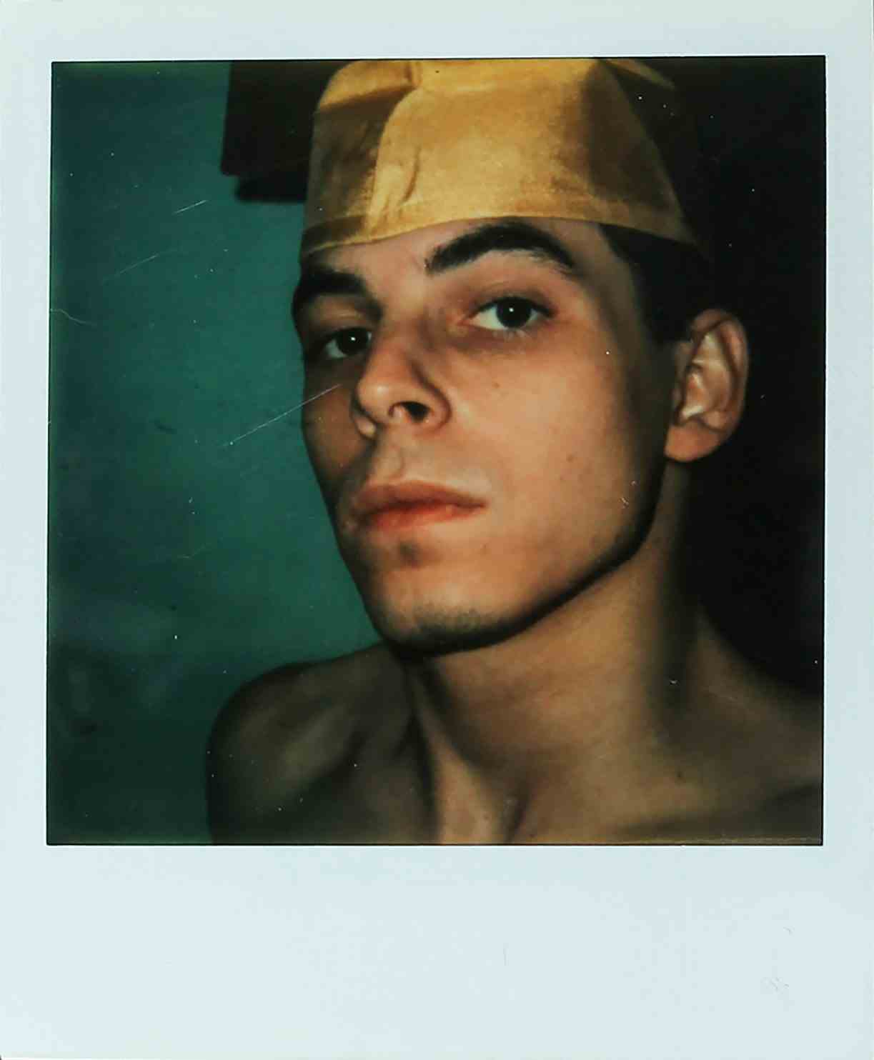 Ein Polaroidfoto einer hemdlosen Person mit Abschlusskappe.