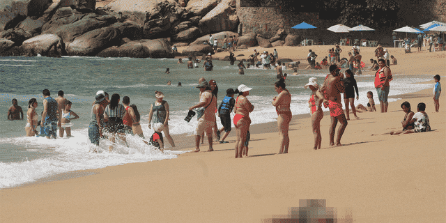 Tourists enjoy the beach near one of three bodies with signs of torture that were washed ashore by the sea, according to local media, at Icacos beach, in Acapulco, Mexico Nov. 12, 2022. 