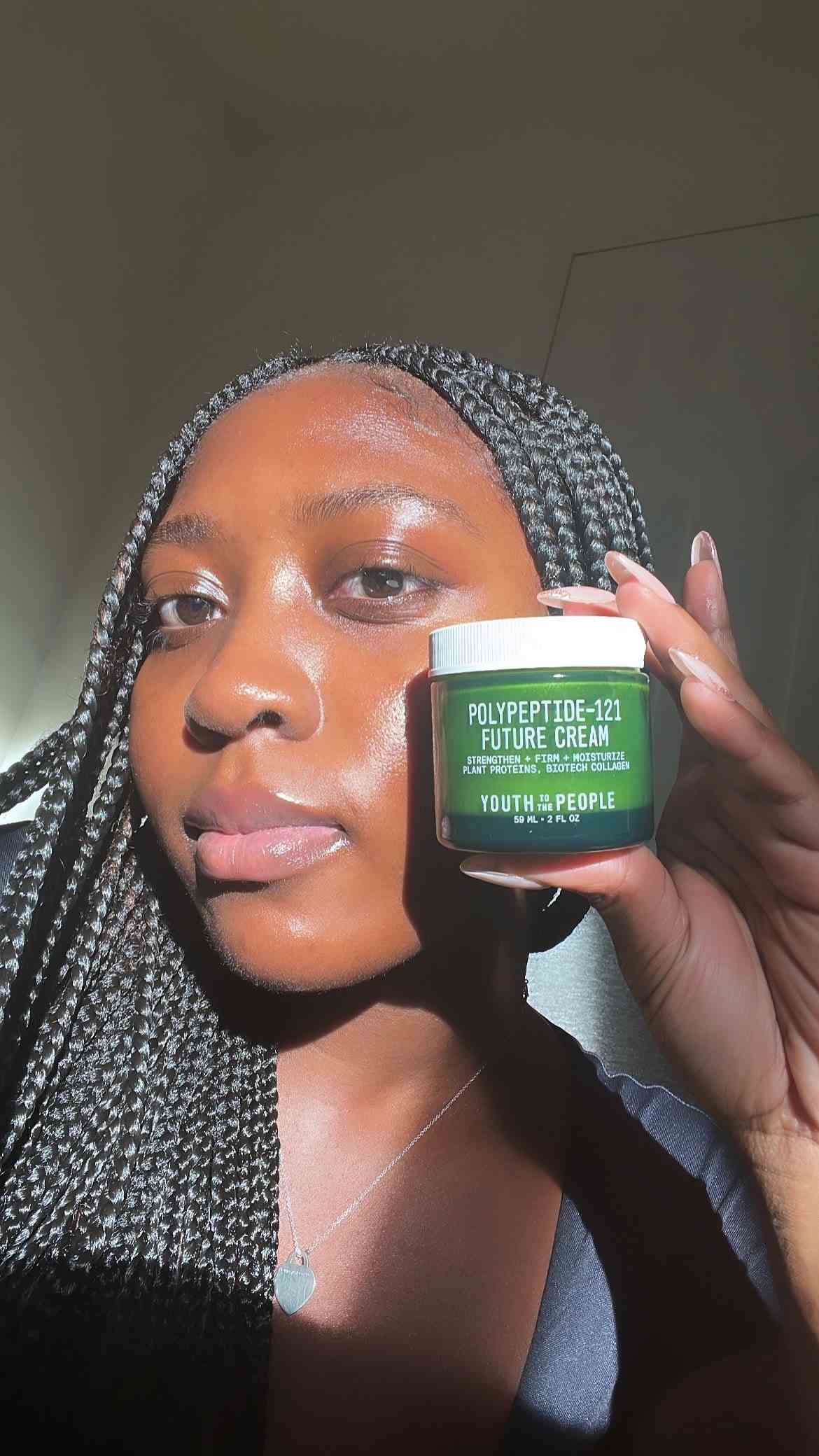 A selfie of Allure associate editor Annie Blay with glowing skin modeling and holding a green jar of Youth to the People...