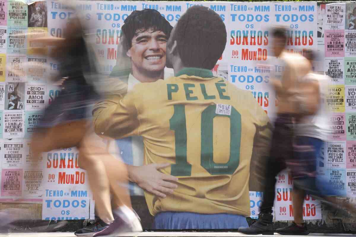 Menschen gehen an einem Wandbild vorbei, das die brasilianische Fußballlegende Pelé zeigt, die den verstorbenen argentinischen Fußballstar Diego Maradona umarmt.