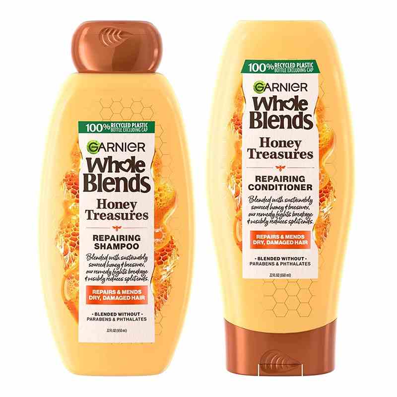 Garnier Whole Blends Honey Treasures Repairing Shampoo and Conditioner zwei gelbe Flaschen mit Bronzekappen auf weißem Hintergrund