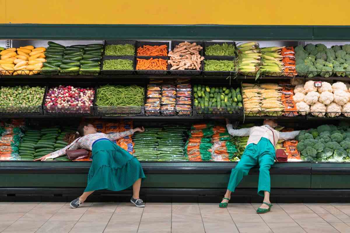 Zwei Frauen breiten sich in einem Supermarktregal über Gemüse aus.