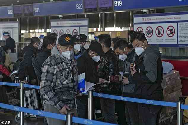 Maskierte Reisende kontrollieren heute ihre Pässe, wenn sie sich am Check-in-Schalter des Beijing Capital International Airport anstellen