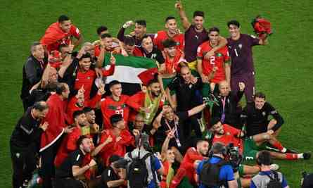 Eine Gruppe von Spielern in roten Hemden versammelt sich für ein Foto auf dem Spielfeld und gestikuliert zum Feiern.  Mehrere Spieler halten in der Mitte der Gruppe die Palästina-Flagge hoch